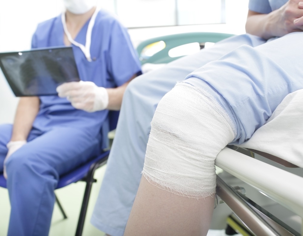 A person with a bandaged knee in a hospital in the USA. A doctor is holding an X-ray.
