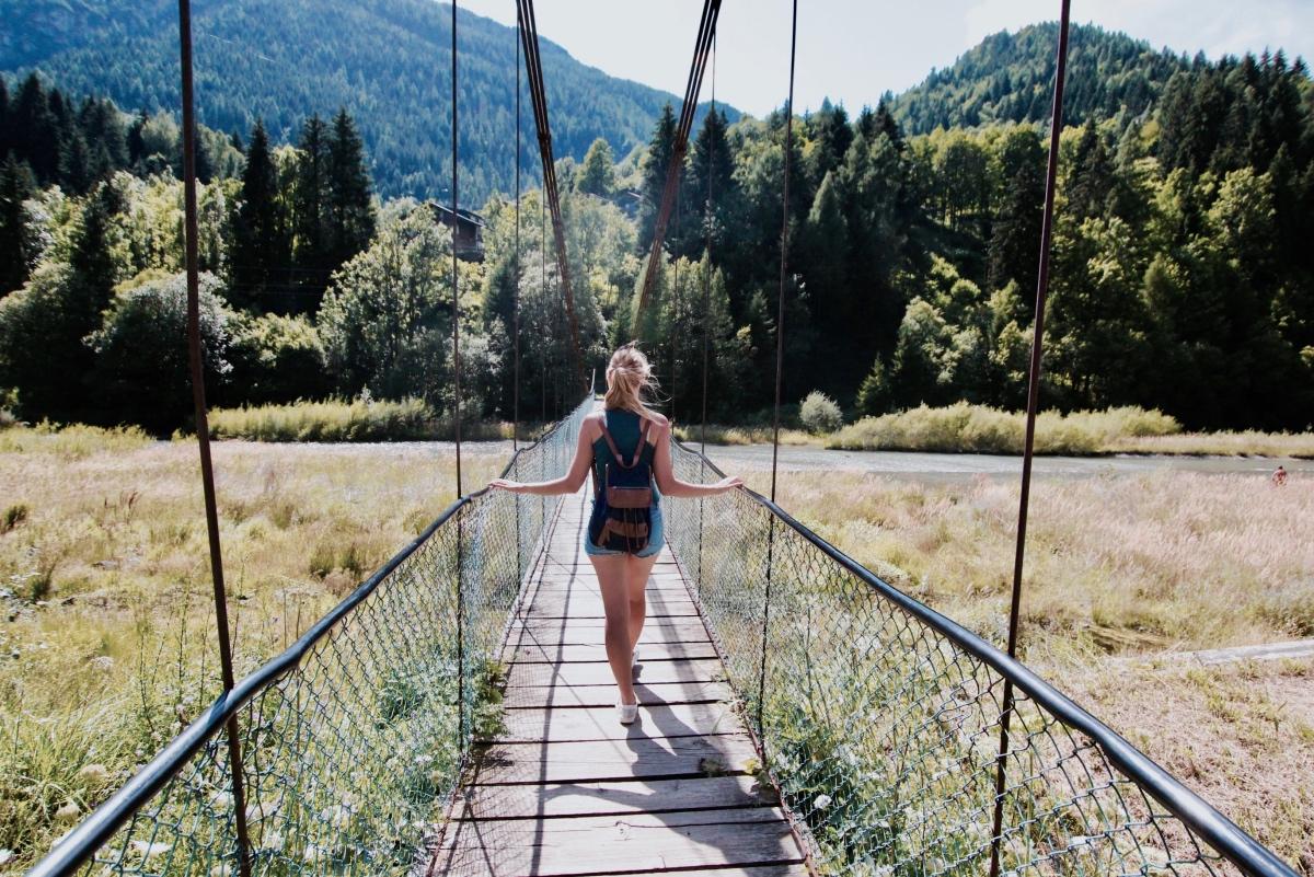 solo female traveller crossing a river on a suspension bridge