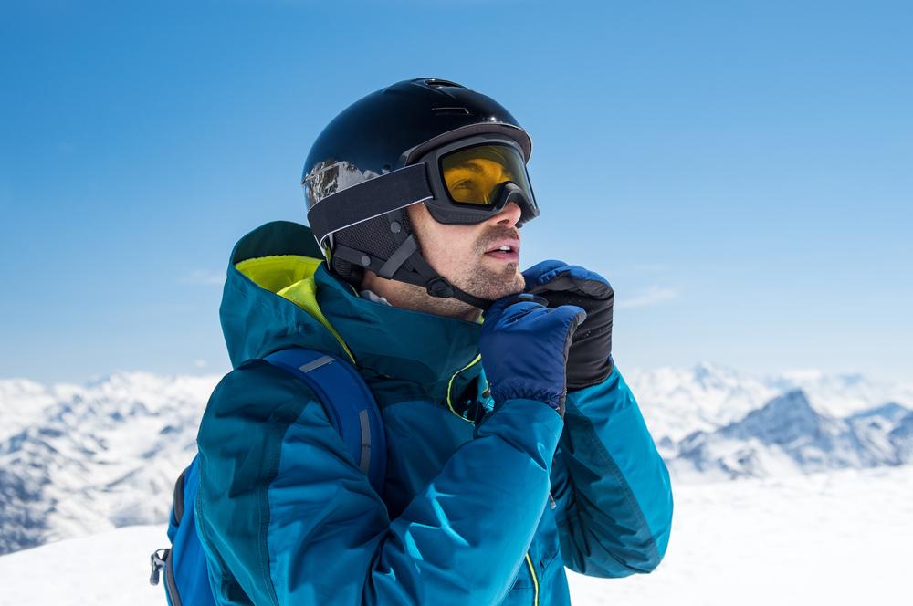 Adult in the mountains, fastening their ski helmet.
