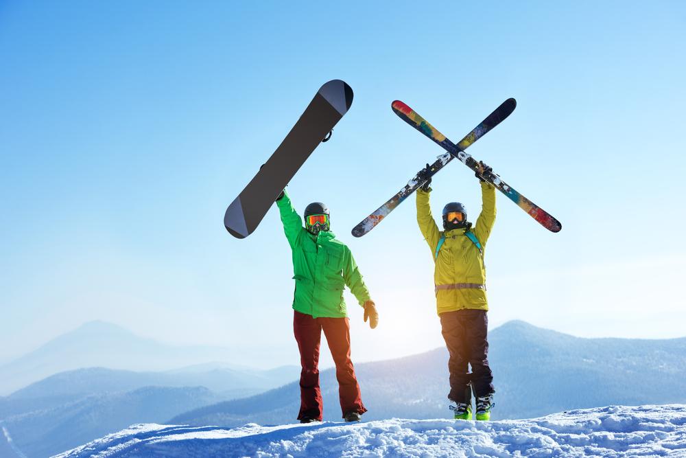 People on a mountain holding skis and a snowboard