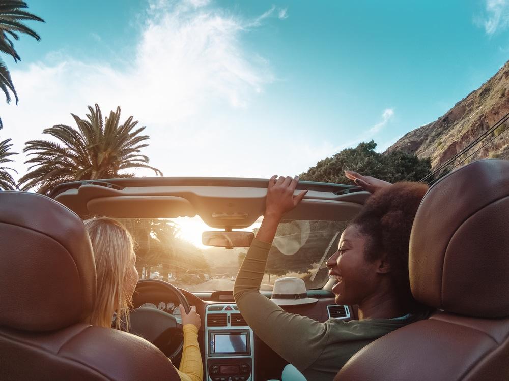 young women driving a rental car, road with palm trees