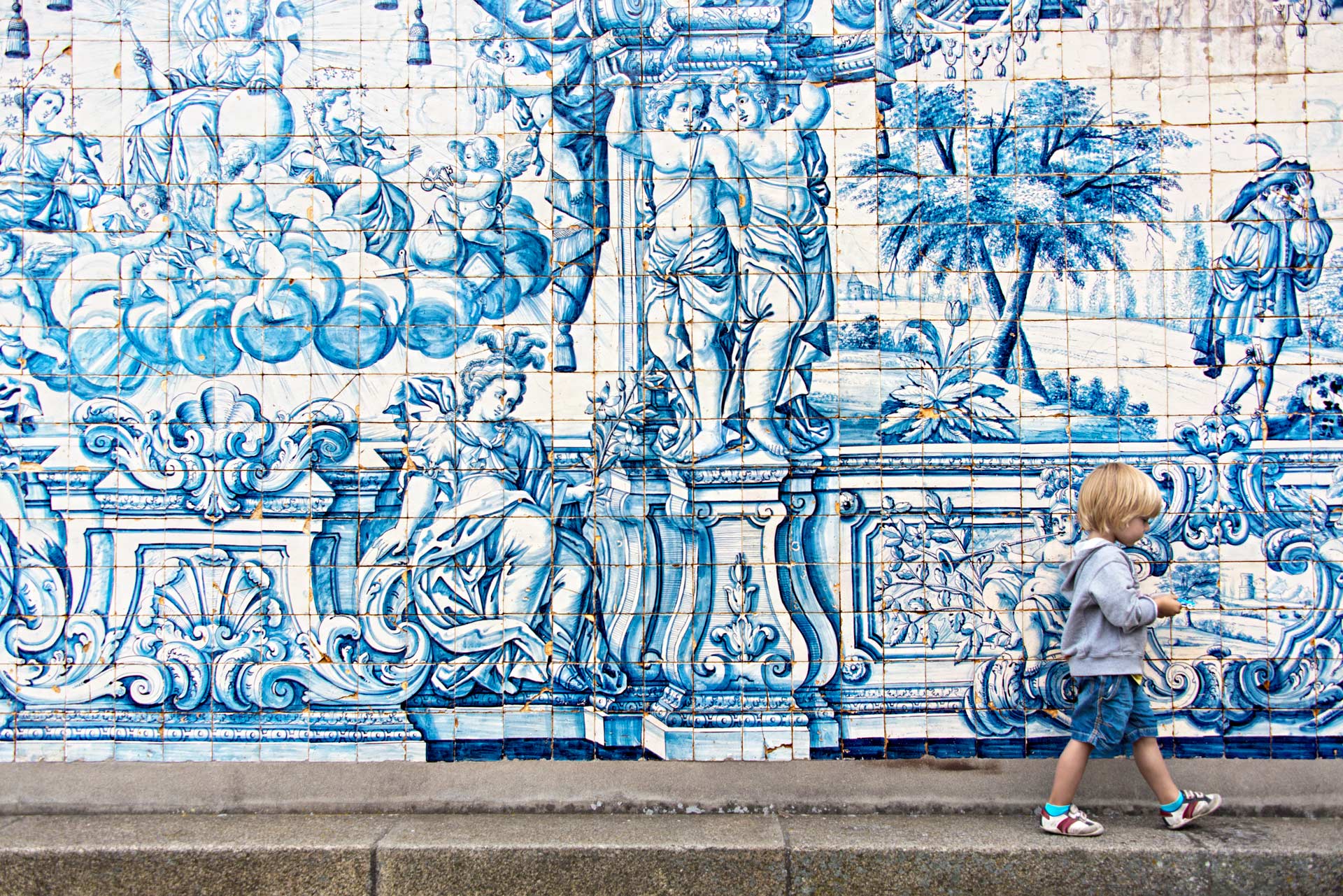a child walking in front of a wall covered in azulejo tiles in Porto